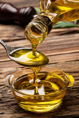 Sürahiden ahşap masada cam kaseye organik zeytin yağı dökülüyor.