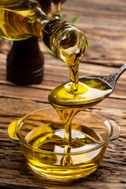 Sürahiden ahşap masada cam kaseye organik zeytin yağı dökülüyor.