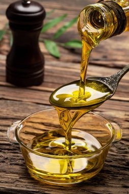 Sürahiden ahşap masada cam kaseye organik zeytin yağı dökülüyor.