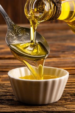 Sürahiden ahşap masada cam kaseye organik zeytin yağı dökülüyor.