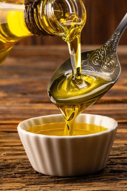 Sürahiden ahşap masada cam kaseye organik zeytin yağı dökülüyor.