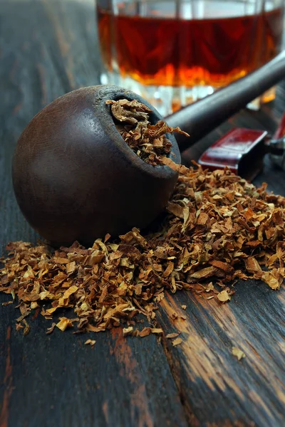smoking pipe with tobacco and a glass of whiskey on a wooden table. top view