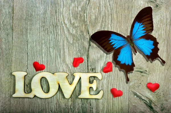 symbols of love. word love, red hearts and bright blue tropical butterfly on a wooden board.