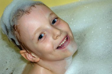 Çocuk küvette köpükle banyo yapıyor.