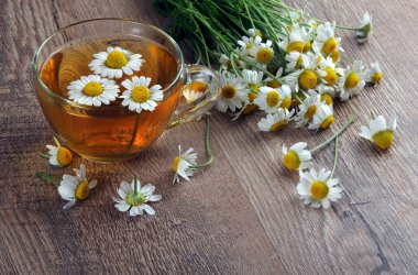 Tahta bir masada cam bir fincanda bitkisel papatya çayı. şifalı bitkiler