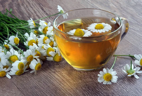 Tahta bir masada cam bir fincanda bitkisel papatya çayı. şifalı bitkiler