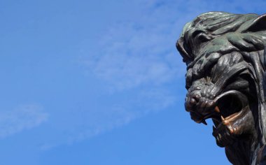 Mavi gökyüzüne karşı bronz bir aslan heykeli. Boşluğu kopyala