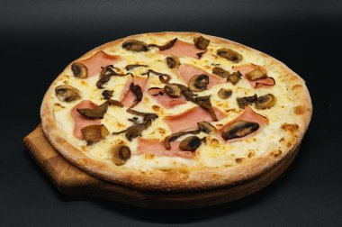 Siyah arka planda tahta bir tahtada jambonlu ve mantarlı pizza.