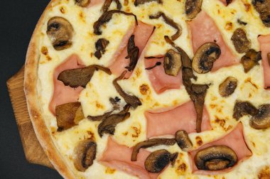Siyah arka planda tahta bir tahtada jambonlu ve mantarlı pizza.