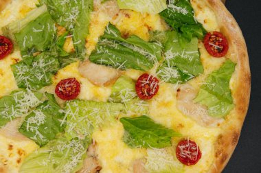 Lezzetli taze sezar pizza. Tavuklu ve sebzeli. Tahta tahtada, siyah arka planda.