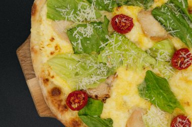 Lezzetli taze sezar pizza. Tavuklu ve sebzeli. Tahta tahtada, siyah arka planda.
