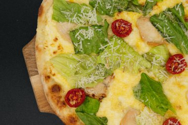 Lezzetli taze sezar pizza. Tavuklu ve sebzeli. Tahta tahtada, siyah arka planda.