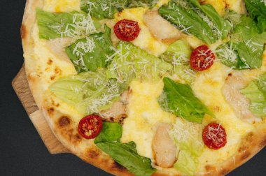 Lezzetli taze sezar pizza. Tavuklu ve sebzeli. Tahta tahtada, siyah arka planda.