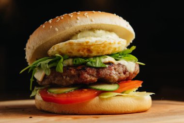 Haşlanmış yumurtalı sığır burger yakın plan. Hamburger - çörek, ızgara et burger, roka salatası, domates ve kızarmış yumurta..