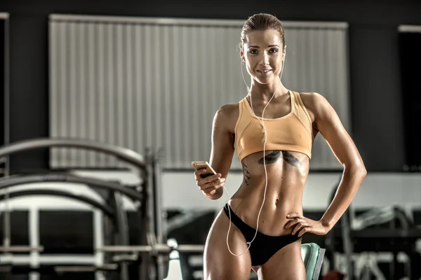 Jeune femme de fitness fatigué dans la salle de gym et écouter de la musique avec casque — Photo