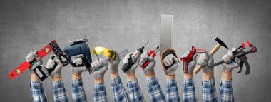 Gri duvar arka planında ahşap işçiliği ve mobilya montajı ve inşaat veya onarım için bir inşaat aracı tutan el grubu