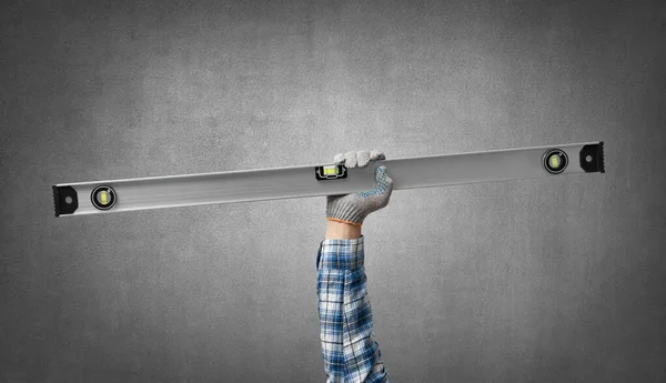 hand holds a construction tool - big spirit level, on gray concrete wall background. Industrial concept
