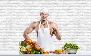 Beyaz toque blanche 'lı erkek vücut geliştirici ve beyaz duvar arkasında koruyucu önlük, karışık sebze ve meyve pişirici. Sağlıklı yeme kavramı