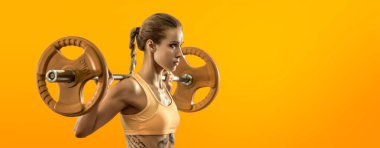 Genç fitness kadını turuncu arka planda ağırlık halteriyle egzersiz yapıyor. Spor salonu konsepti