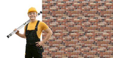 İnşaat ruhuna sahip mutlu işçi tamirci ya da inşaatçı, tüm vücudunu siyaha boğ - sarı üniforma içinde dur ve tuğla duvar arkasında gülümse. Onarım ve inşaat konsepti