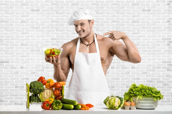白いトークのブランチで男のボディビルダーと調理保護エプロン 調合野菜や果物 白いレンガの壁の背景に 健康的な食事のコンセプト — ストック写真