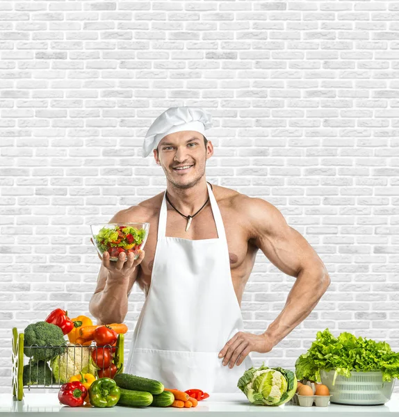 白いトーキーのブランチで男のボディビルダーと料理の保護エプロン 調合野菜や笑顔 白いレンガの壁の背景にあります 健康的な食事のコンセプト — ストック写真