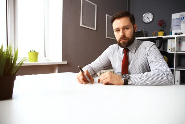 Selbstbewusster junger Mann am Laptop, während er an seinem Arbeitsplatz im Büro sitzt — Stockfoto