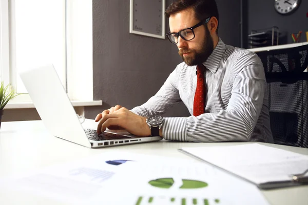 Selbstbewusster junger Mann am Laptop, während er an seinem Arbeitsplatz im Büro sitzt — Stockfoto