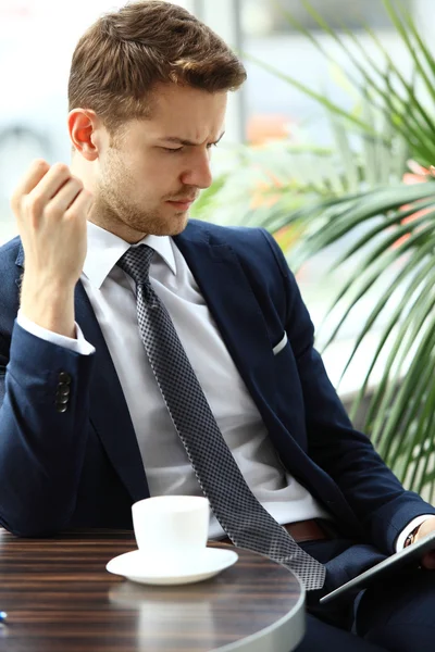 Retrato de hombre guapo y exitoso beber café y mirar a la pantalla de la tableta digital sentado en la cafetería —  Fotos de Stock