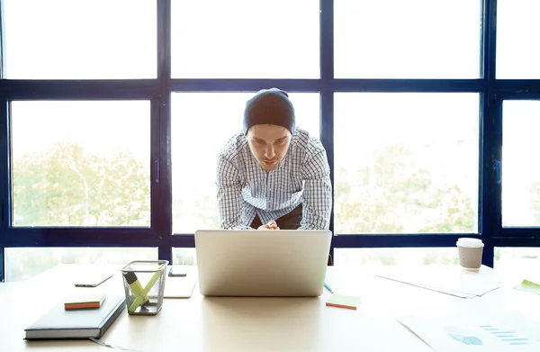 Pensive młody przystojny człowiek pracuje na laptopie siedząc w swoim miejscu pracy — Zdjęcie stockowe