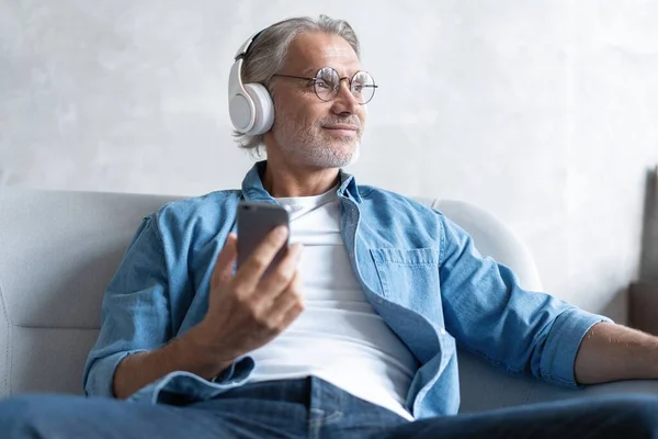 Homem em casa no sofá ouvindo uma música com um smartphone. — Fotografia de Stock