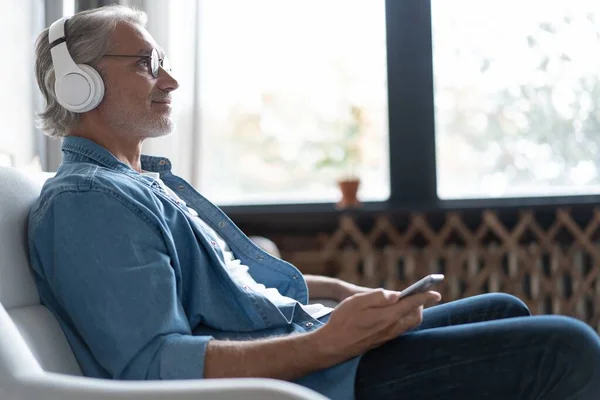 Hombre en casa en el sofá escuchando una música con un smartphone. — Foto de Stock