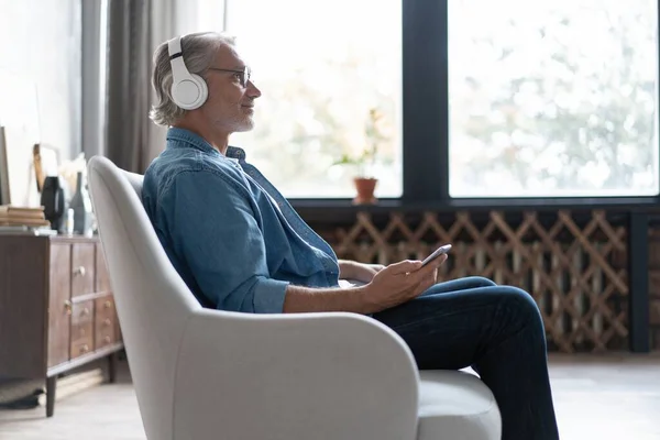 Hombre en casa en el sofá escuchando una música con un smartphone. — Foto de Stock