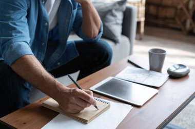 Evdeki kanepede otururken günlük giysiler içinde mali belgelerle çalışan bir adam..