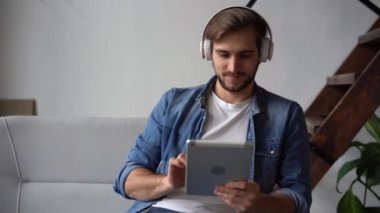 Kulaklıklı çekici bir genç adam evdeki tabletten video izliyor.