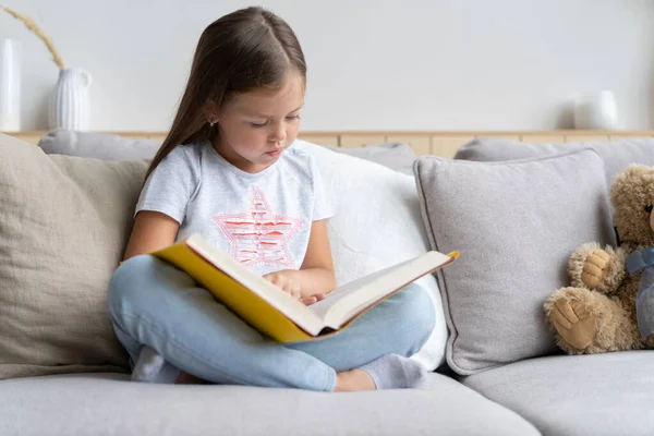 Młoda dziewczyna czyta książkę w domu. Kształcenie na odległość, edukacja domowa. Koncepcja samodzielnej izolacji. — Zdjęcie stockowe