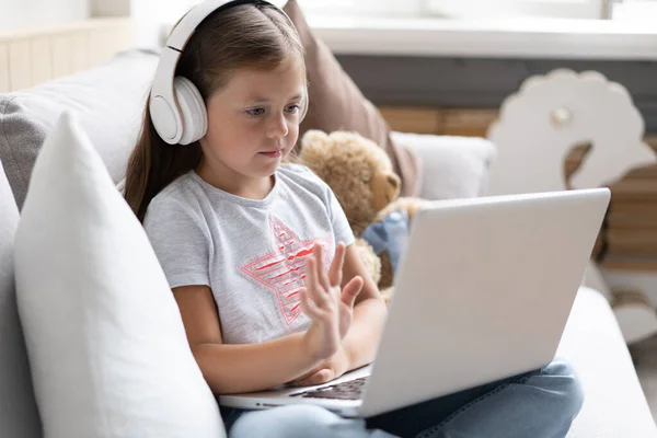 Online eğitim. Kulaklıklı tatlı kız video dersi öğretmeni konferansı laptopuyla evdeki kanepede oturuyor. — Stok fotoğraf