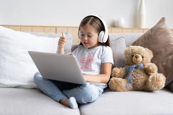 Online education. Sweet girl with headphones looking video lesson teacher conference laptop sitting on the couch at home — Stock Photo, Image