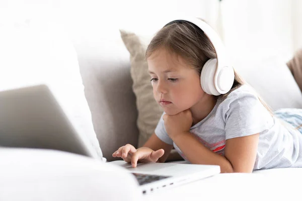 온라인 교육. 헤드폰을 낀 멋진 소녀가 집 소파에 앉아 비디오 수업을 듣고 있습니다. — 스톡 사진