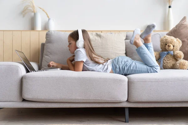 Educación en línea. Dulce chica con auriculares mirando video lección profesor conferencia portátil sentado en el sofá en casa — Foto de Stock