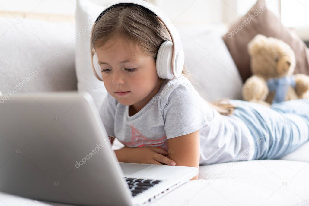 Online education. Sweet girl with headphones looking video lesson teacher conference laptop sitting on the couch at home