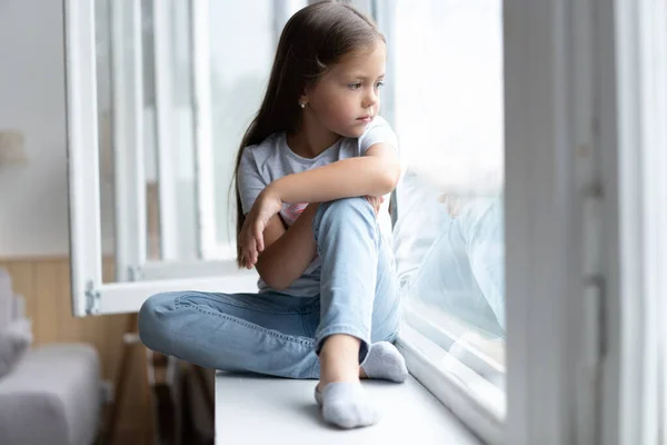 Schönes kleines Mädchen, das aus dem Fenster schaut. Junges Mädchen schaut aus dem Fenster. Fröhliches Kind liegt auf Fensterbank — Stockfoto