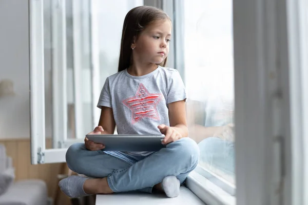 Criança bonita usando um tablet digital em um interior doméstico com grande janela. — Fotografia de Stock