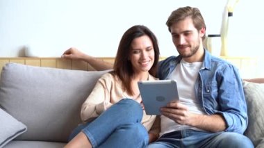 Mutlu genç çift kanepede oturuyor, tablet bilgisayar kullanıyorlar, geziniyorlar, eğleniyorlar.