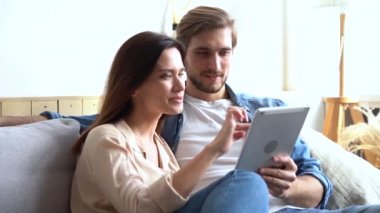 Mutlu genç çift kanepede oturuyor, tablet bilgisayar kullanıyorlar, geziniyorlar, eğleniyorlar.