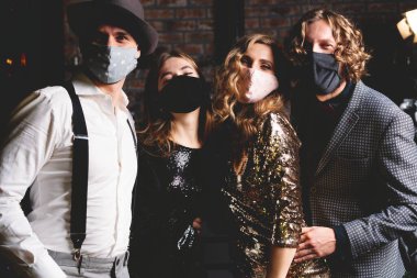 Corona virüsü salgını. Koruyucu maske takmış bir grup güzel genç insan dans ediyor, mutlu görünüyorlar.