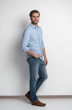 Kot pantolon ve gömlek giymiş sıradan bir gencin stüdyo portresi. Beyaz arkaplanda izole.