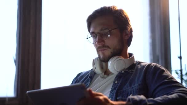 Uomo seduto sul divano a casa, utilizzando gadget, tablet computer, rimanere occupato nel fine settimana. — Video Stock