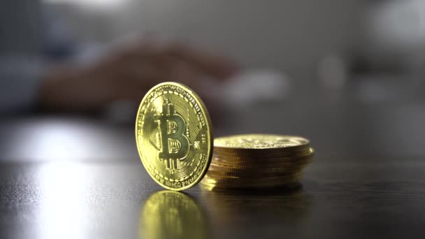 Guld bitcoin mynt på bordet nära affärskvinna arbetar på datorn — Stockvideo