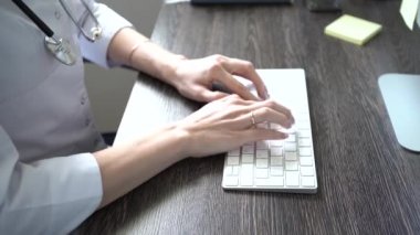 Bilgisayarda daktilo eden bir doktor, yakın plan. Doktor hastaların elektronik dosyalarını dolduruyor.